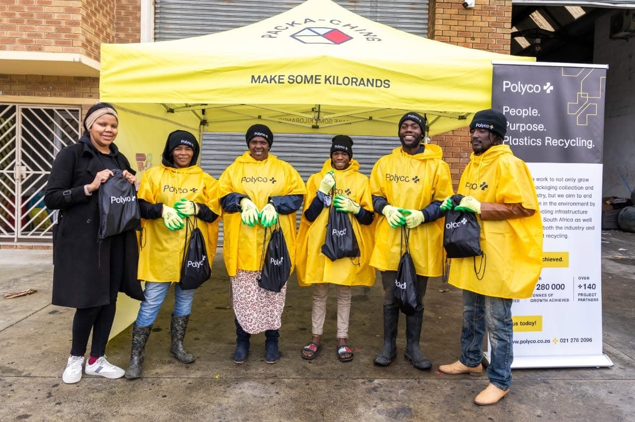 A large team of WasteGo Green and Polyco collectors in yellow ponchos gathered under a ‘Make Some Kilorands’ Packa-Ching gazebo outside the Milnerton depot