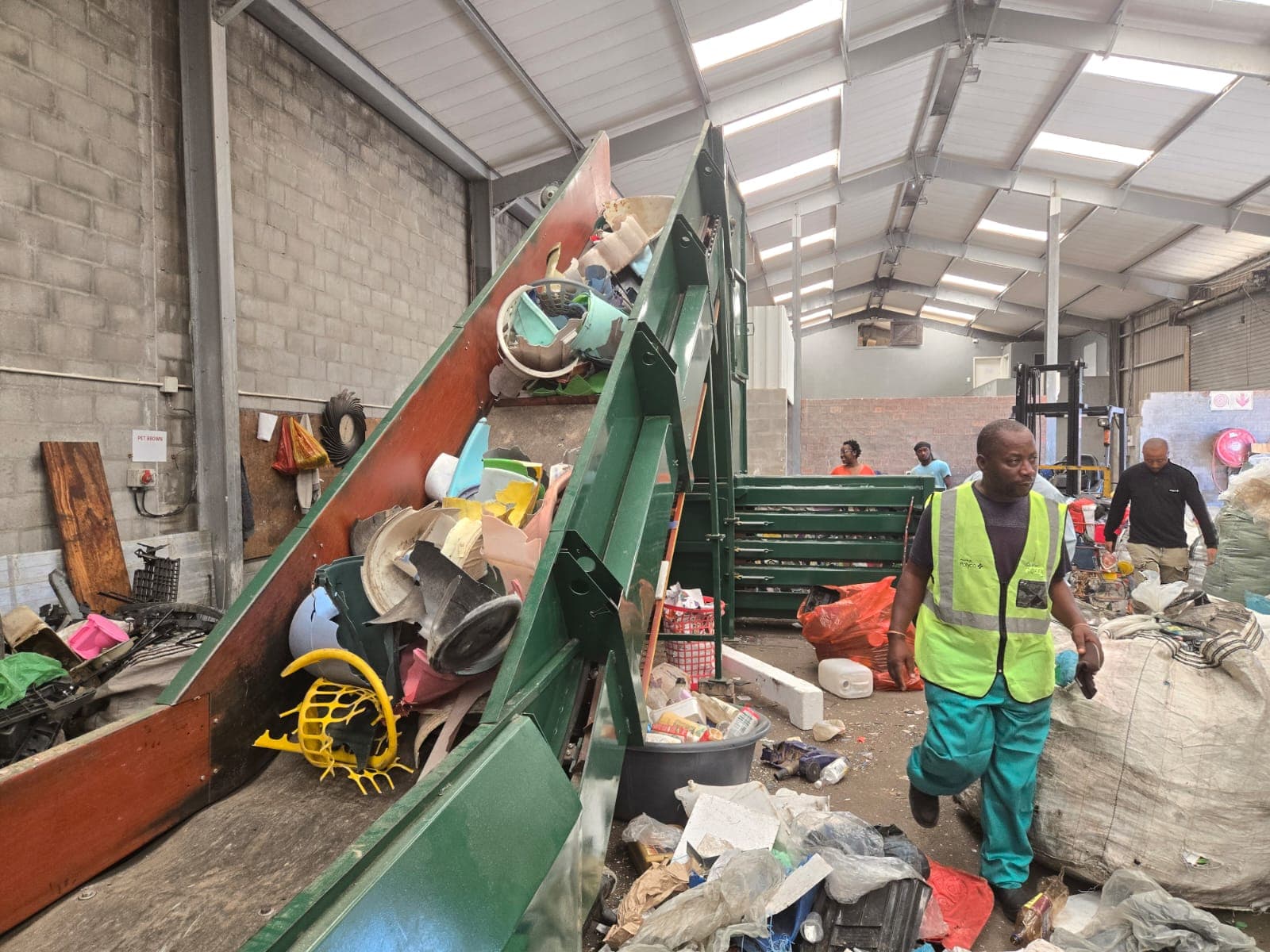 Worker in a hi-vis vest beside an inclined sorting conveyor feeding mixed plastics inside the WasteGo Green materials recovery facility